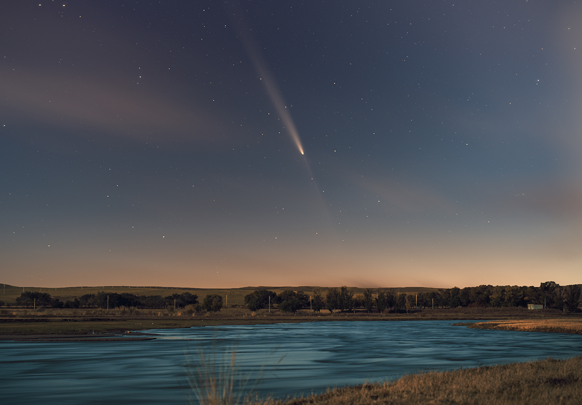 A comet moves across the night sky above a river.
