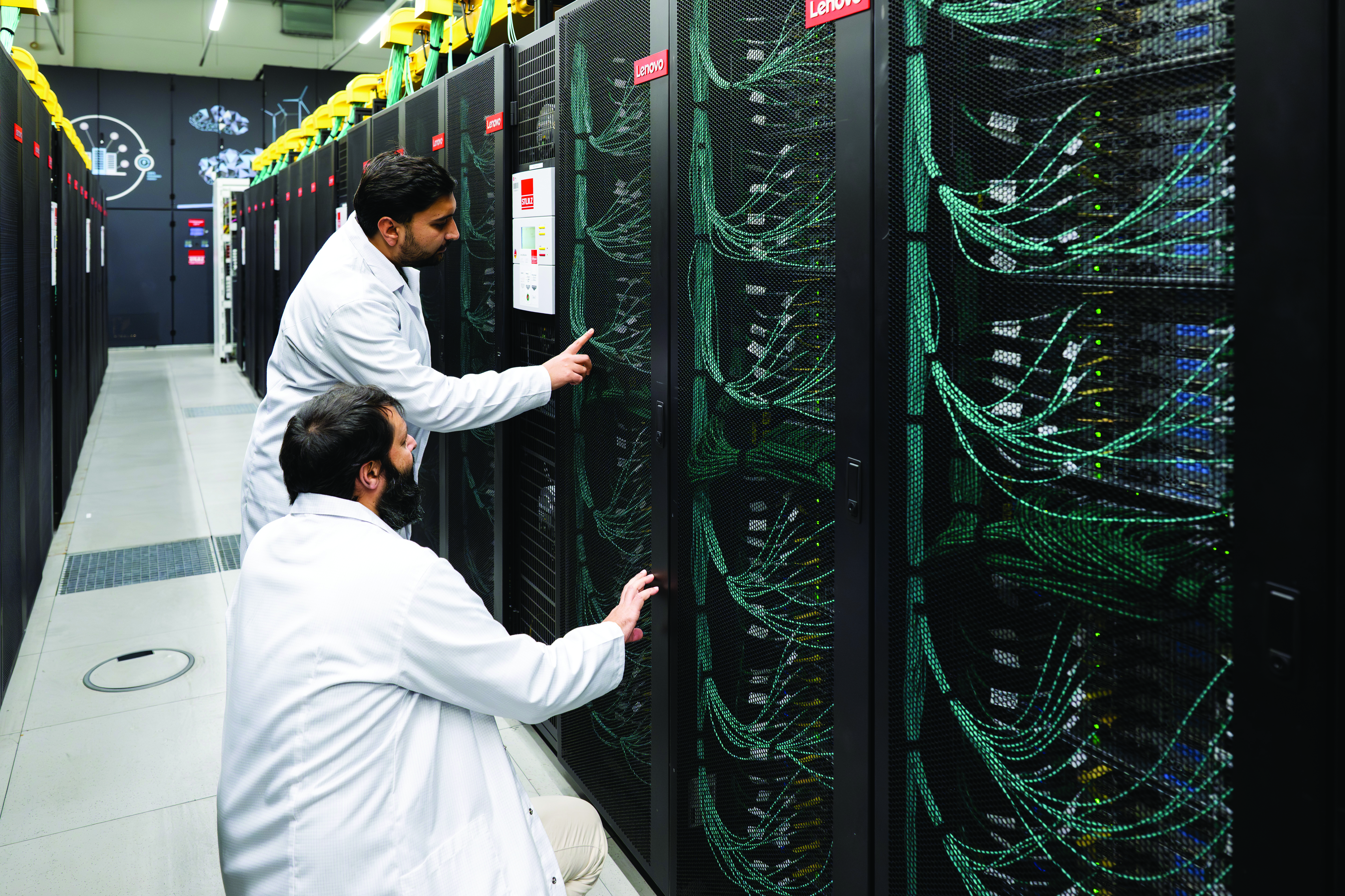Two scientists in white coats examine components of a large supercomputer.