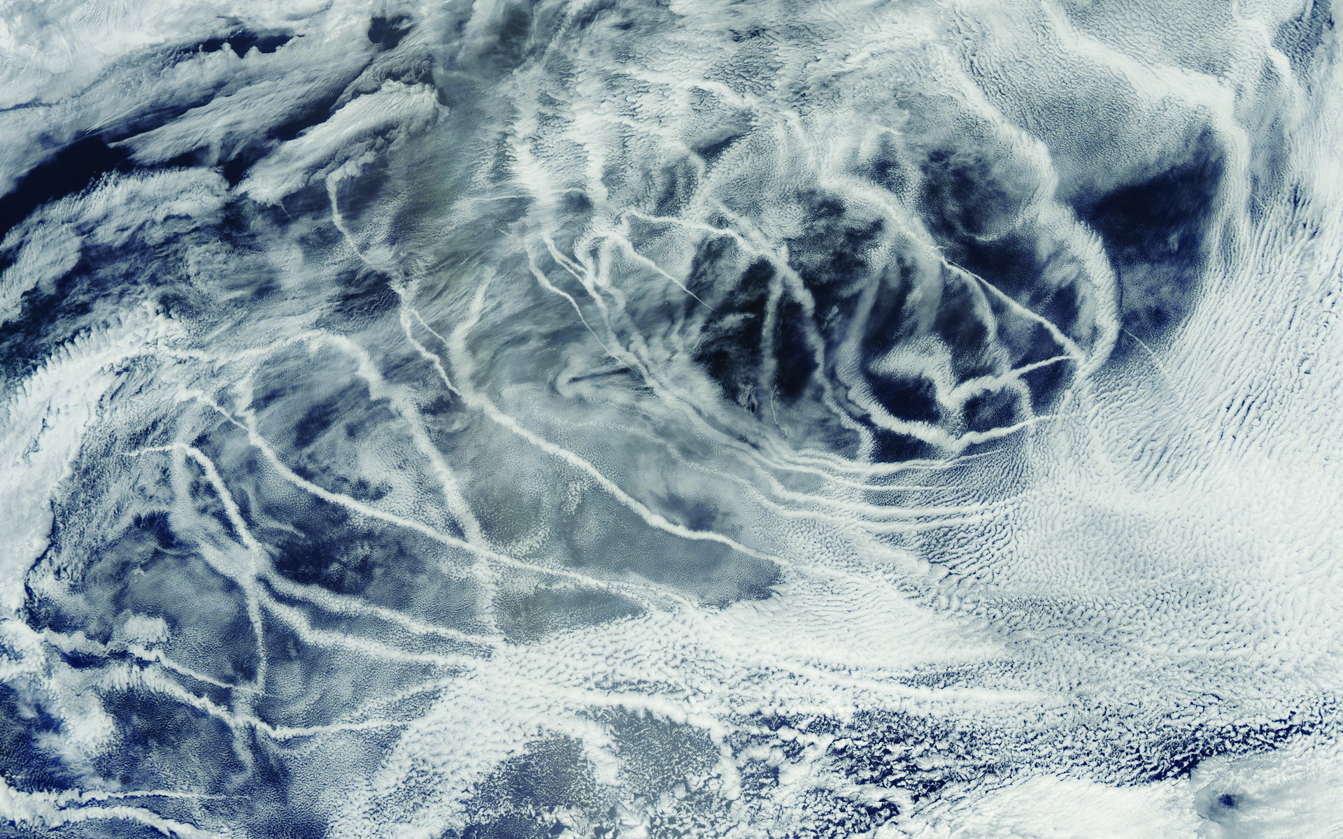 An aerial view of rope-like clouds crisscrossing over a dark blue ocean.