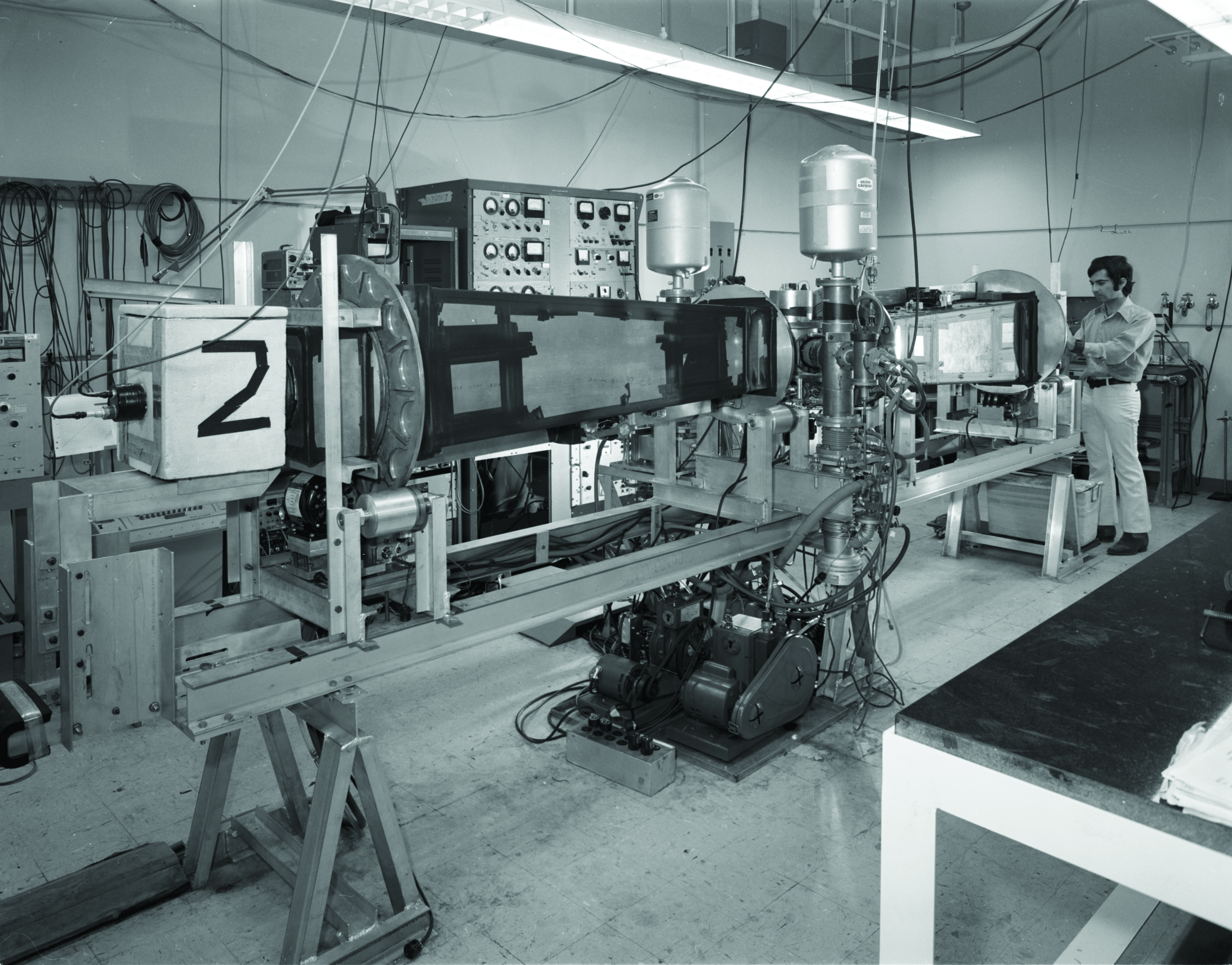 Alt text: A man standing next to a long apparatus in a lab.