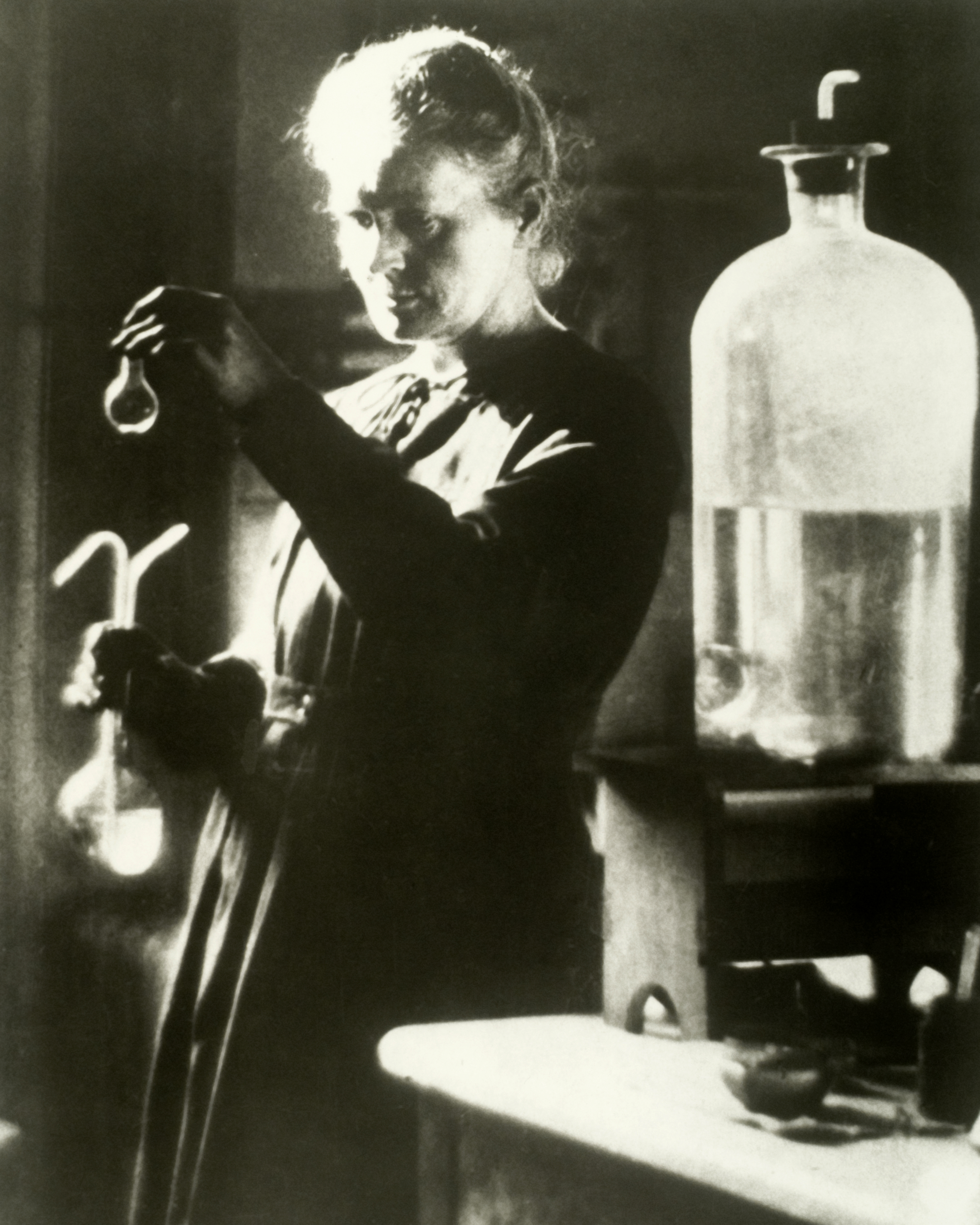 Marie Curie holds a up a vial in a lab.