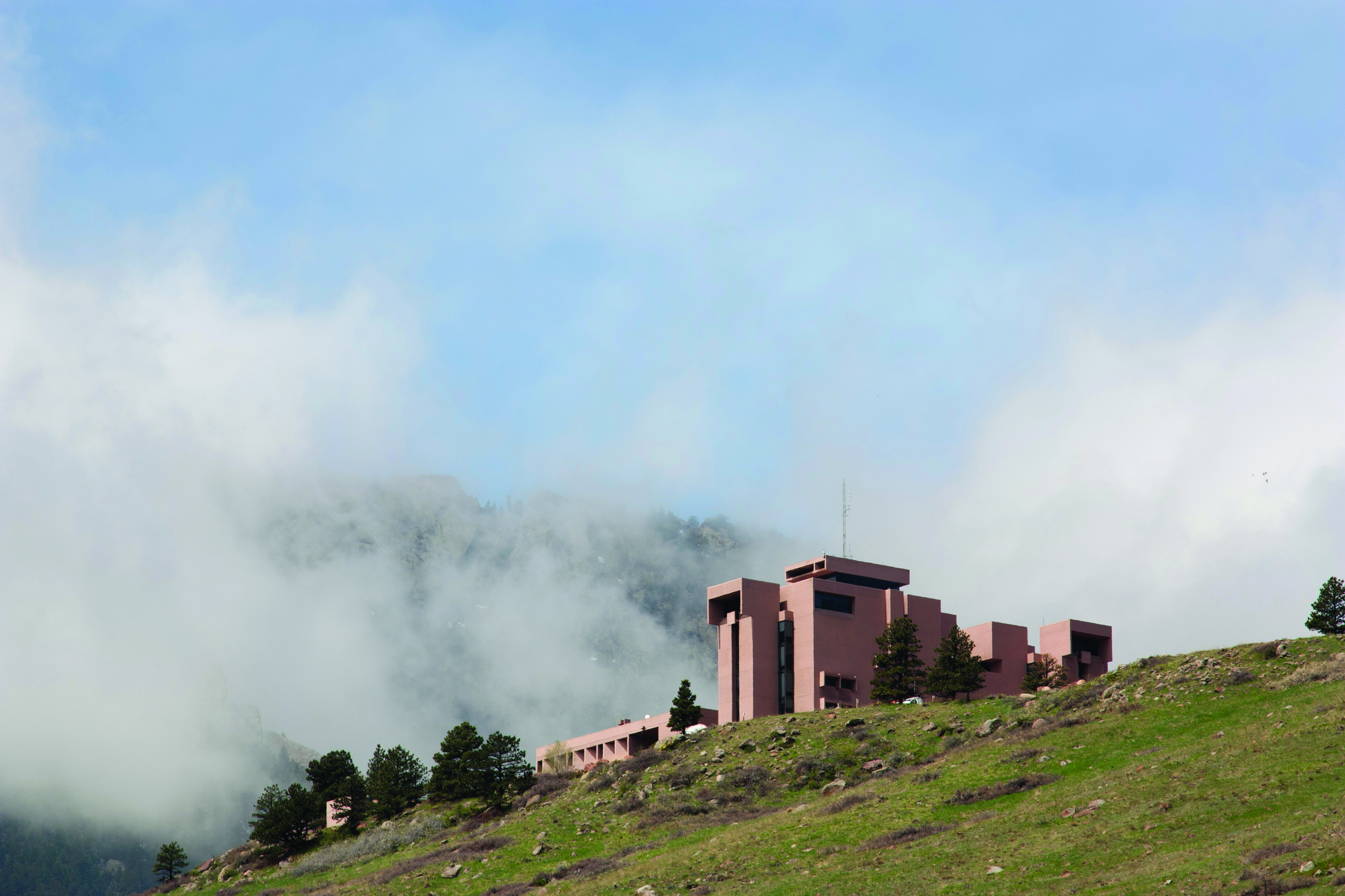 A building on a mesa with clouds and a mountain in the background.