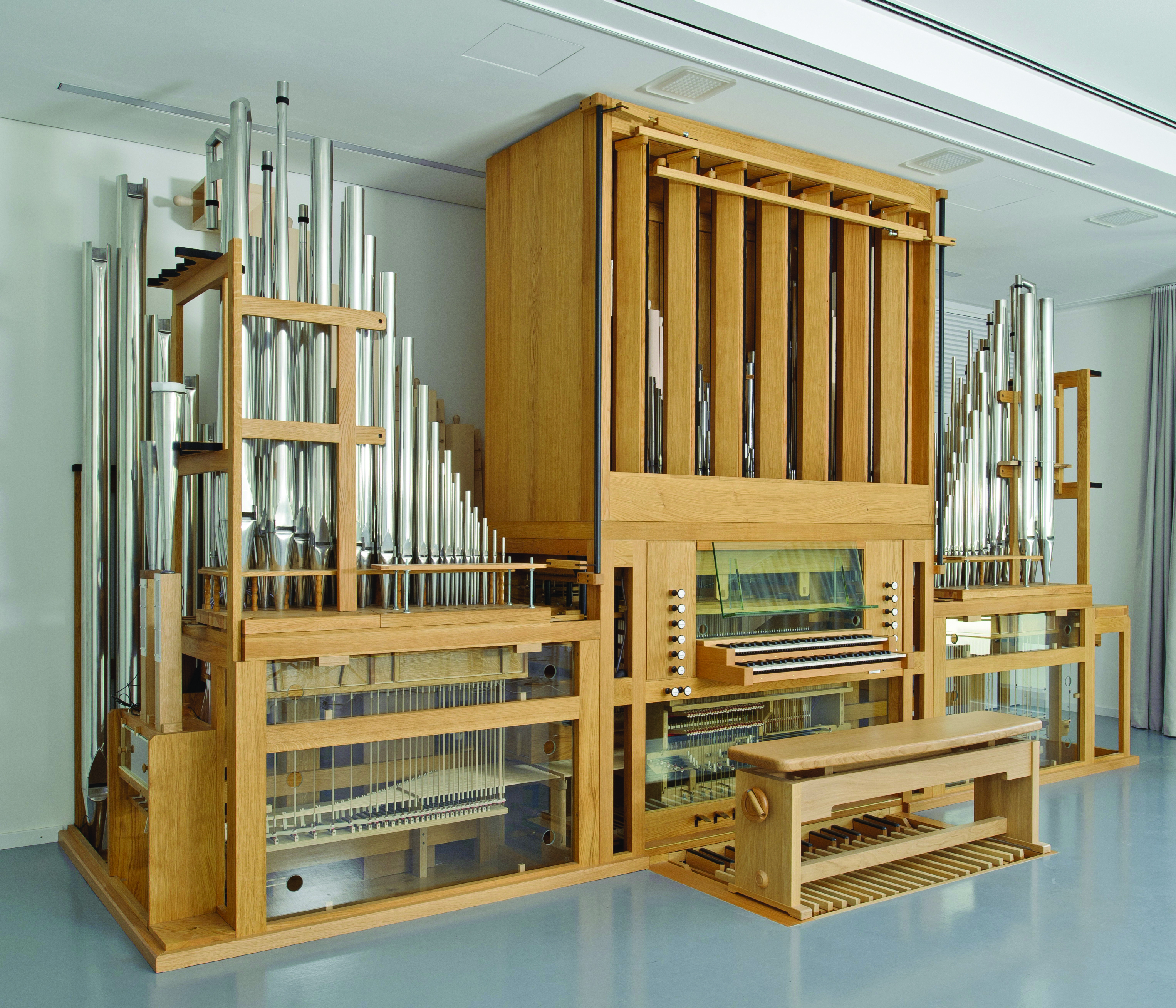 A small pipe organ, with pipes, keyboard, pedalboard, and knobs to control the stops that are used. Many of the components are housed in glass cases.