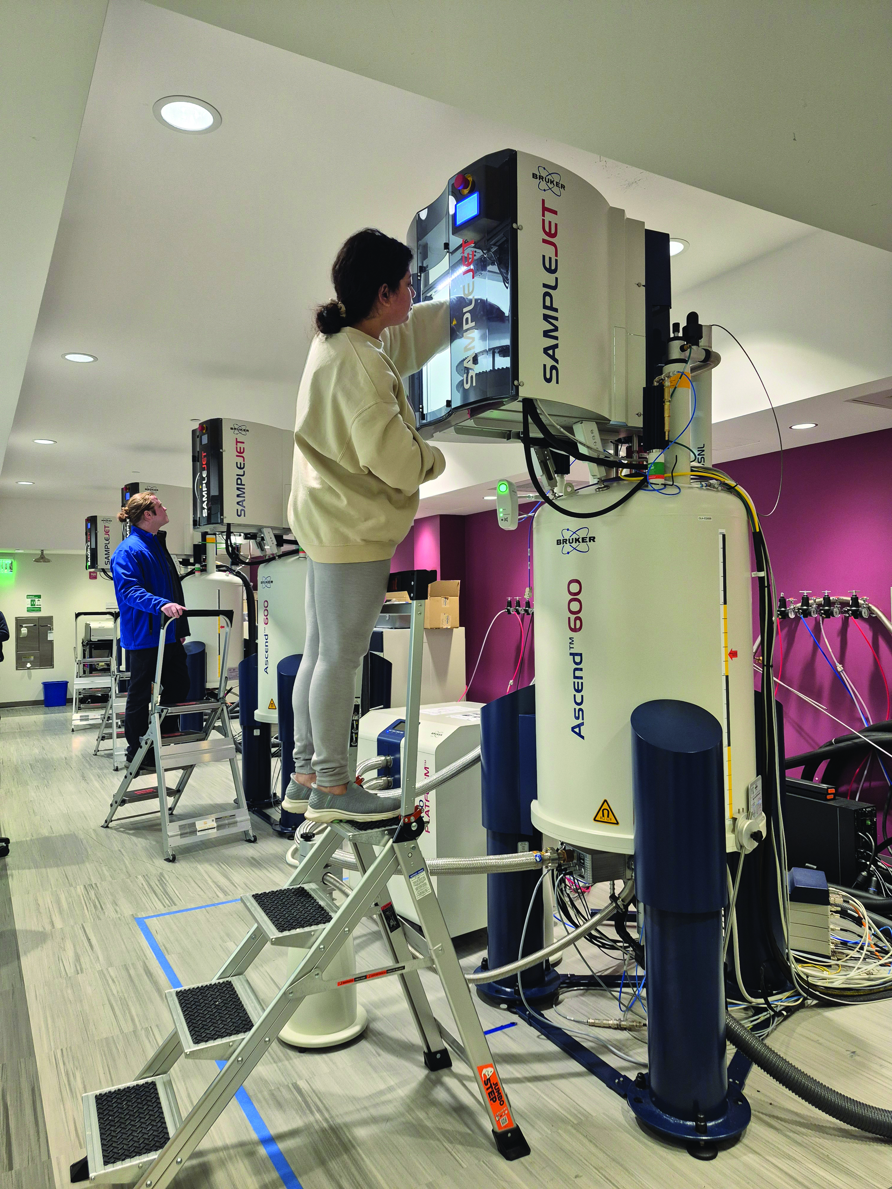 A woman places a sample into an NMR spectrometer.