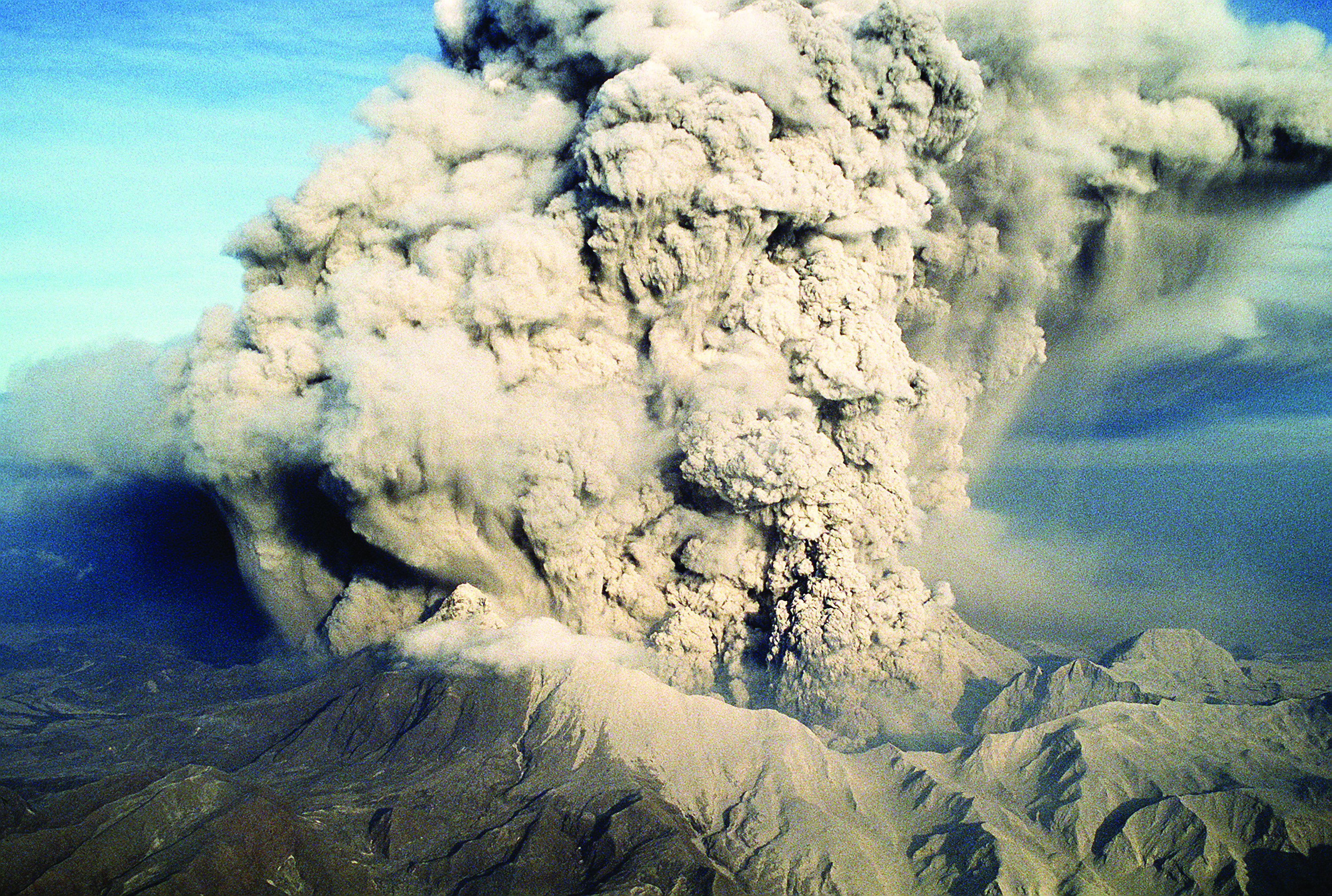 A large cloud of ash erupts from a volcano, as seen from the sky.