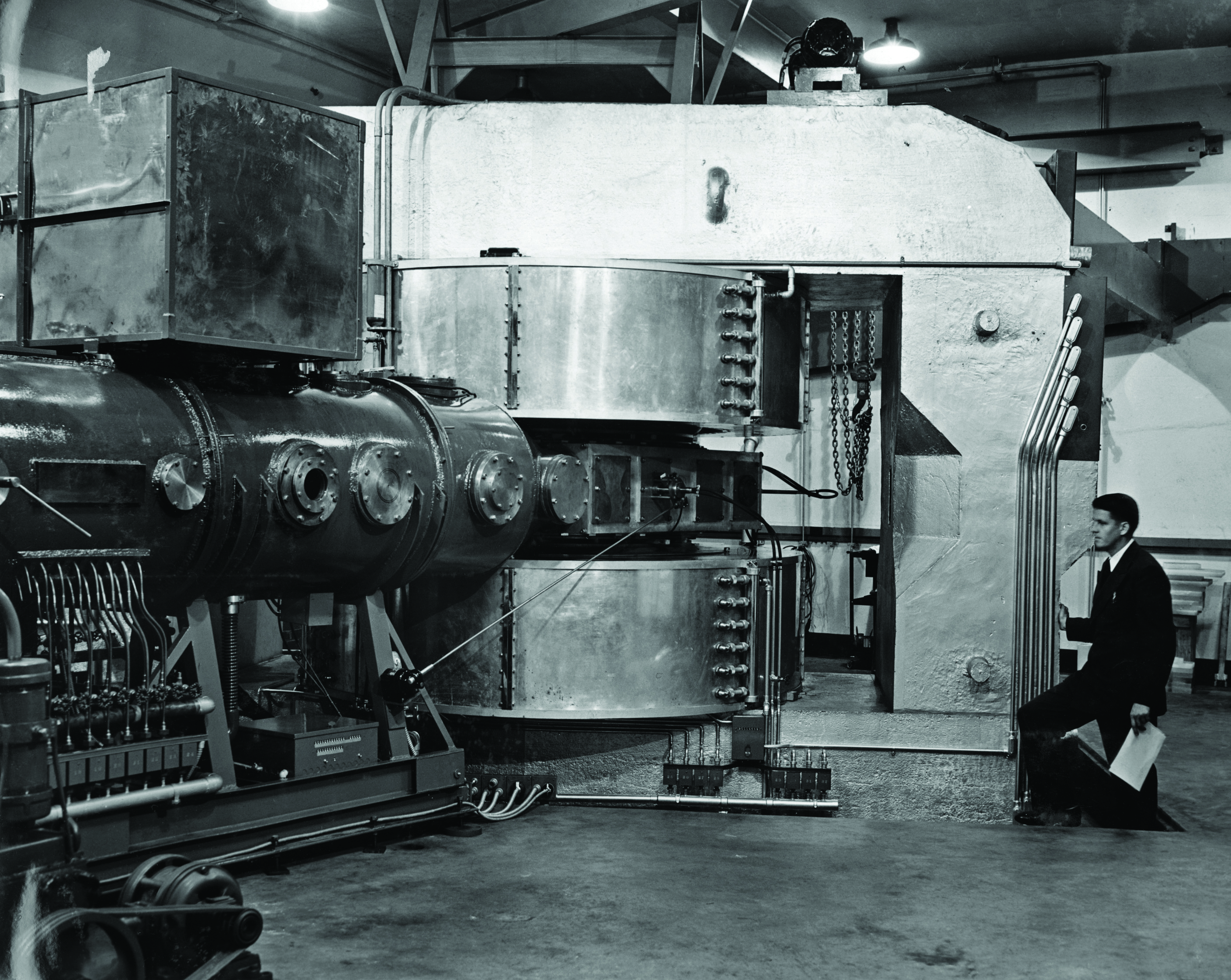 A man kneels beside a room-size metal apparatus.
