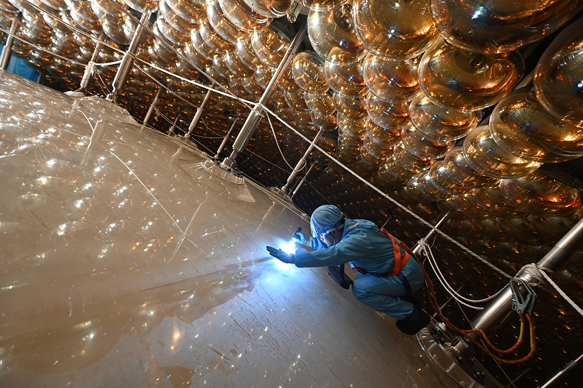 A person kneeling shines a flashlight into the spherical neutrino detector.