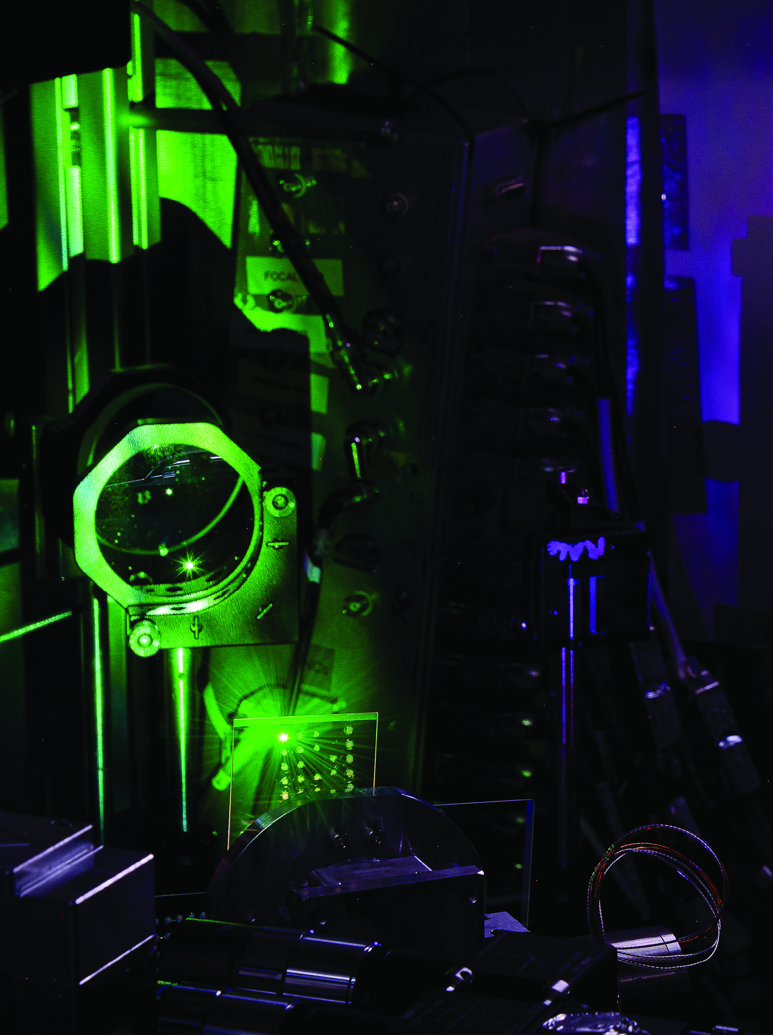 On a lab table, a plate of glass is illuminated by a laser and generates a glowing green plasma. The laser's first harmonic appears purple.