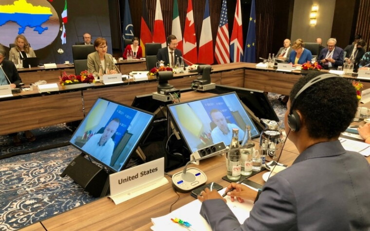 International leaders seated at tables surrounding four display screens. Alondra Nelson is in the foreground, facing away from the camera