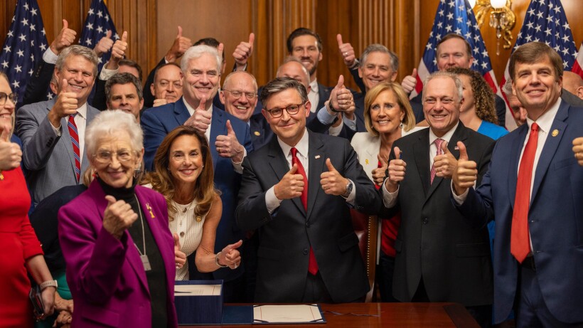 A crowd of people giving a thumbs up in front of four American flags