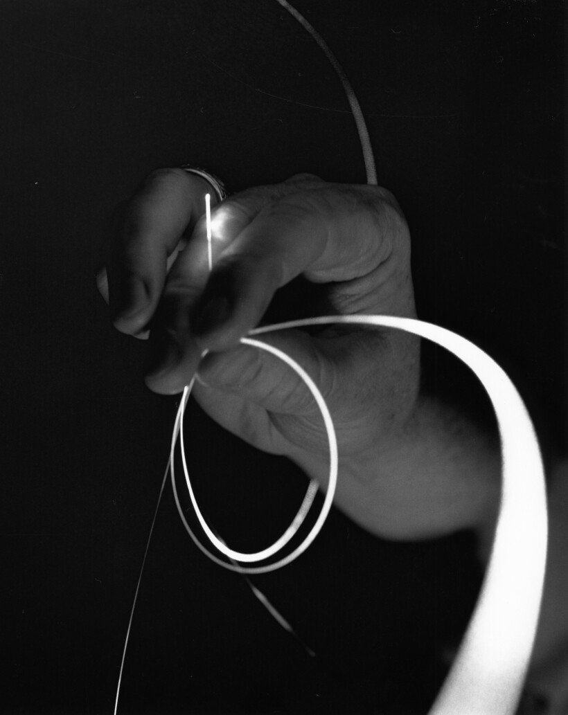 Closeup of a hand holding thin loops of lighted glass fibers.