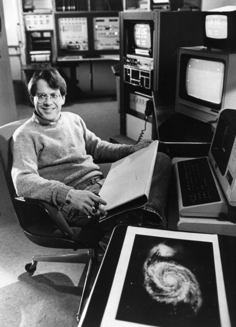 Timothy Ferris sitting in a room with tvs and equipment