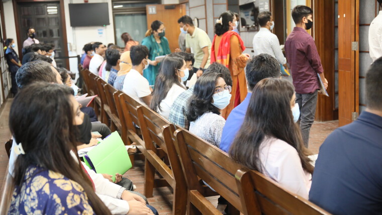A group of people sit in a waiting room with their backs to camera at the US embassy in Dhaka.