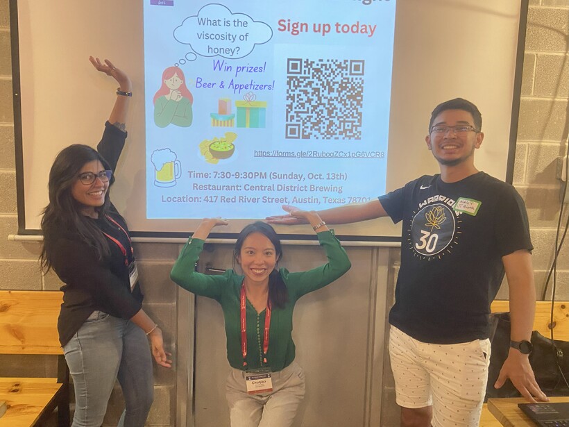 Three people pose in front of a projector screen.