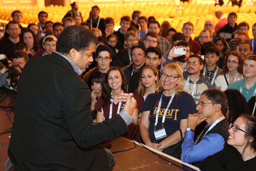 Neil deGrasse Tyson kneels onstage talking to a crowd of people after a presentation at an American Astronomical Society Meeting.