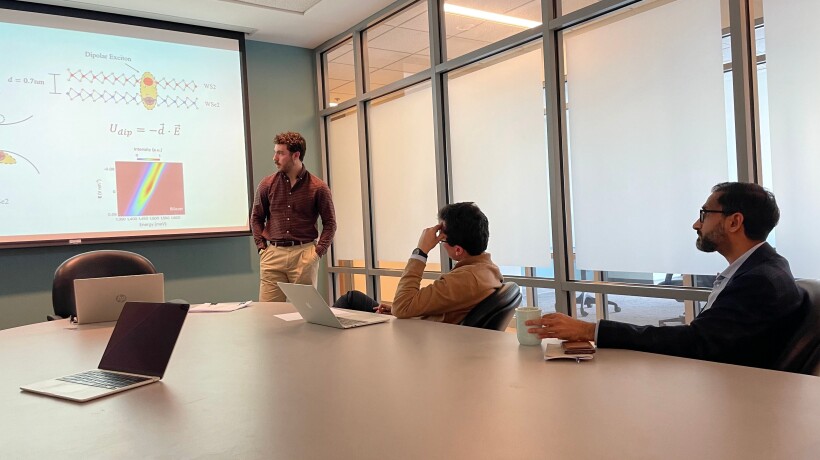 Three people in a room looking at a screen. One is standing and talking, two are looking on.