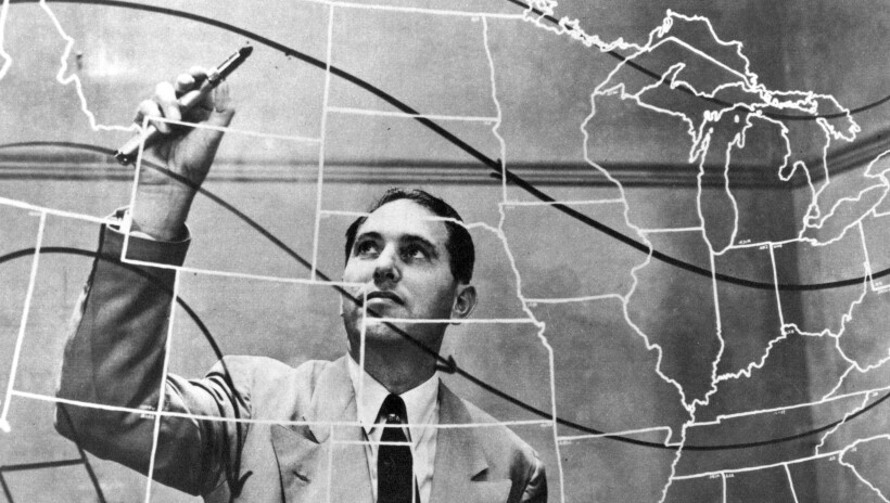 Man behind glass map of USA with pen in hand looking at his hand as he begins to draw