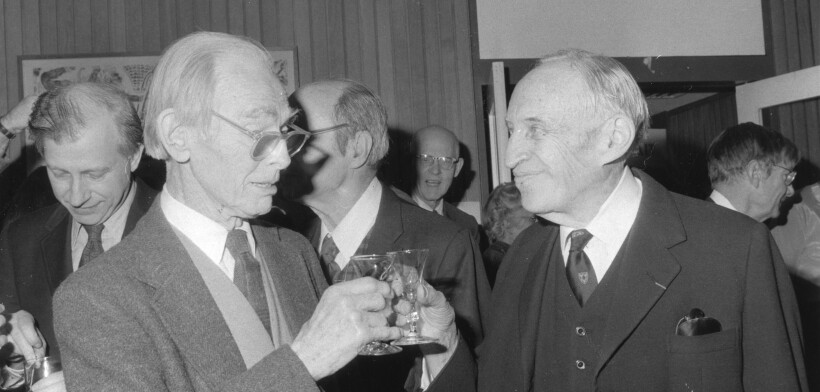 two older men in suits toasting each other in a crowded room