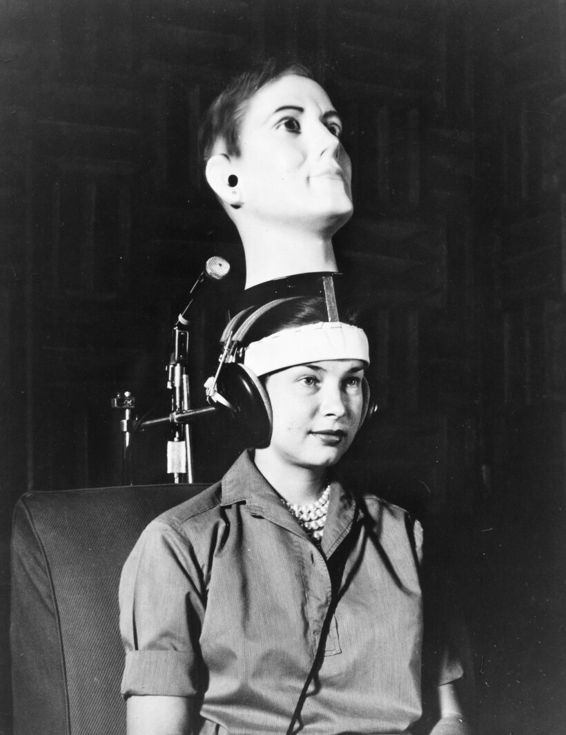 A woman wears a dummy head and headphones as part of an acoustics experiment.