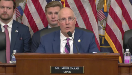 A man with glasses sits behind a microphone