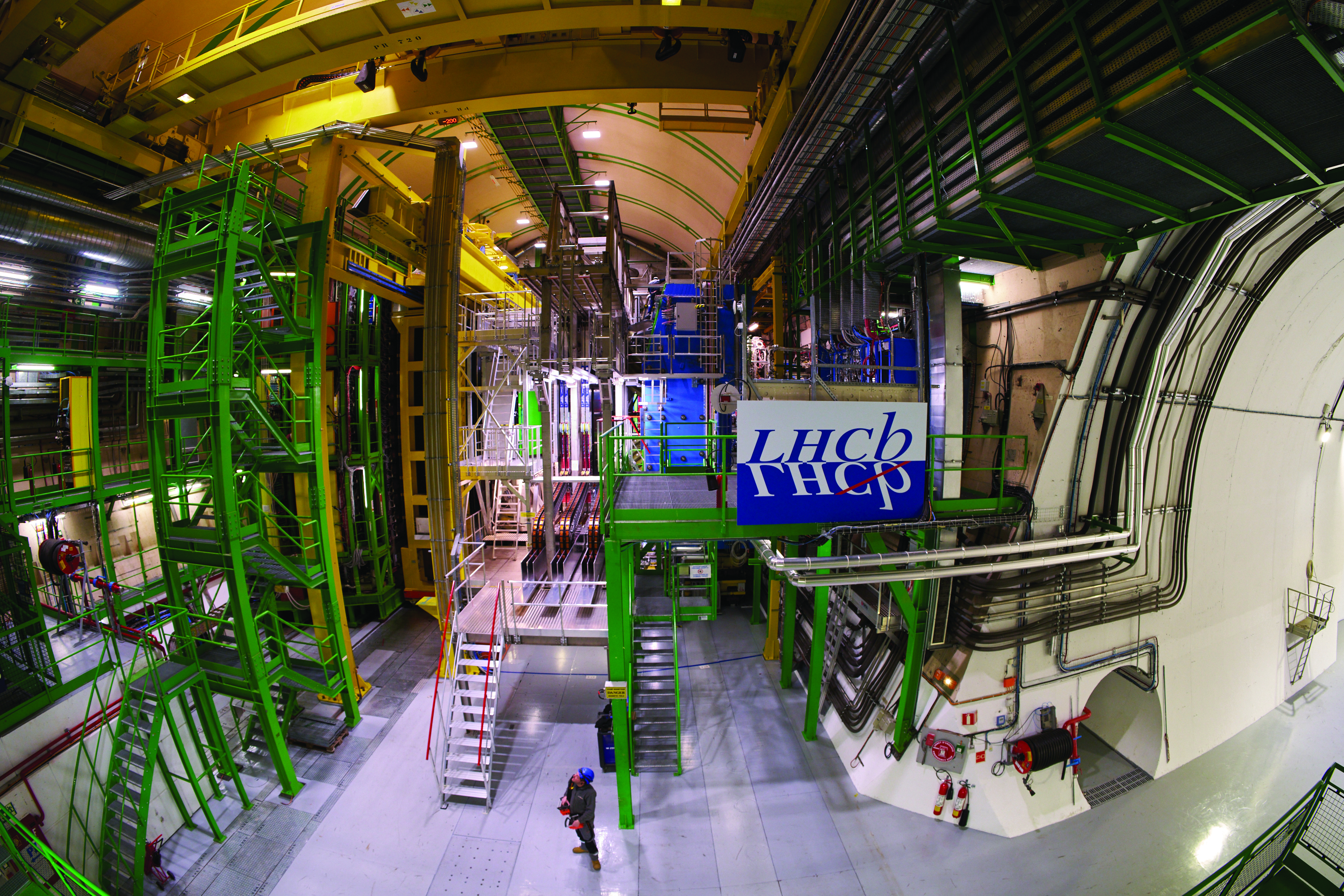 An interior view of the LHCb experiment shows a mixture of yellow and green scaffolding and a sign that says “LHCb.”
